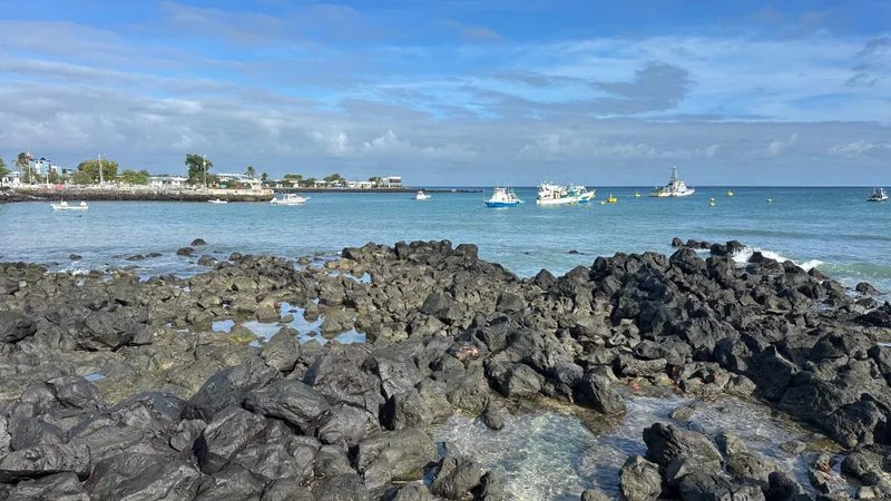 Barcos na baía de Puerto Baquerizo Moreno além da costa vulcânica de San Cristóbal